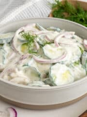 Side view of creamy cucumber salad in a bowl with dill in the background.