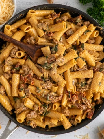 Overhead, look at creamy Tuscan sausage pasta in a skillet.