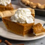 Close-up of a slice of homemade pumpkin pie with a bite taken out of it.