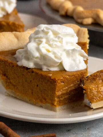 Close-up of a slice of homemade pumpkin pie with a bite taken out of it.