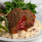 The best meatloaf recipe topped with meatloaf sauce on garlic mashed potatoes.