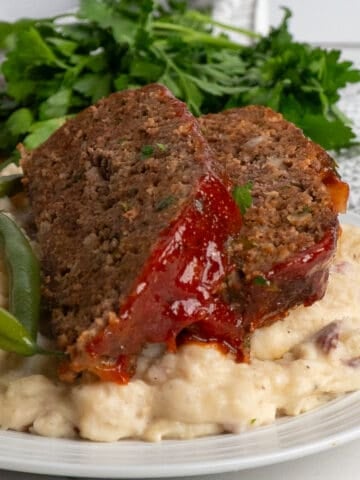 The best meatloaf recipe topped with meatloaf sauce on garlic mashed potatoes.