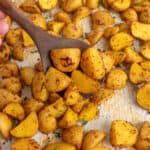 A wooden spoon holding oven roasted Yukon gold potatoes on a sheet pan.