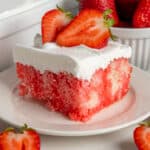 Close-up of strawberry poke cake with fresh strawberries on top.