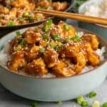 Honey sesame chicken over a bowl of rice and garnished with green onions