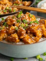 Side view of sesame chicken over a bowl of rice and garnished with green onions