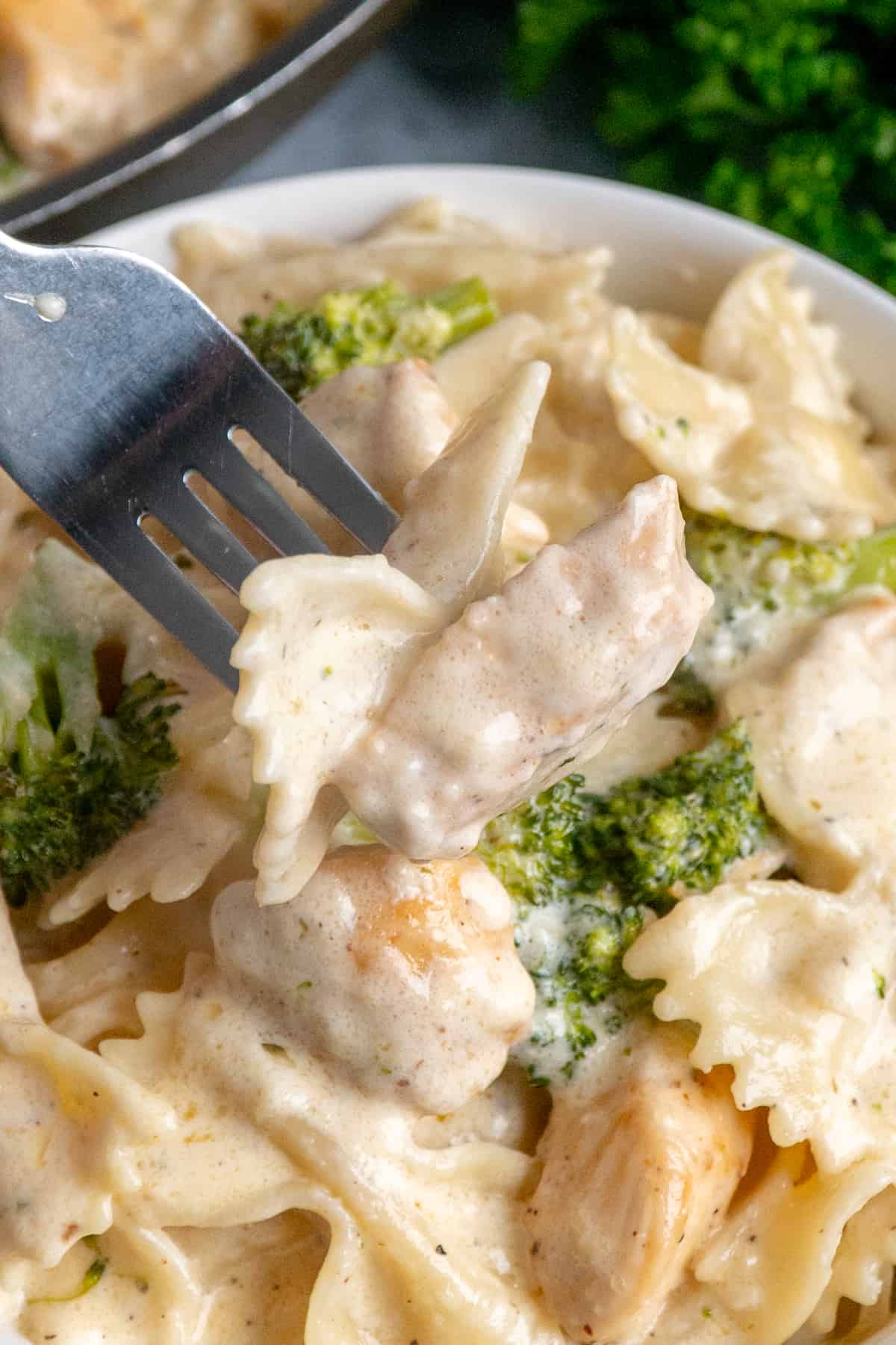 A fork holding a bite of chicken broccoli Alfredo over a bowl.