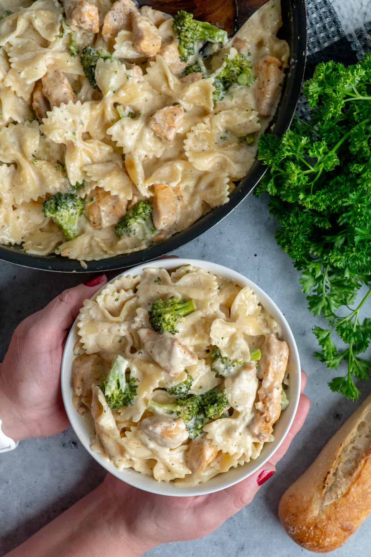 Hands holding a bowl of chicken broccoli Alfredo.