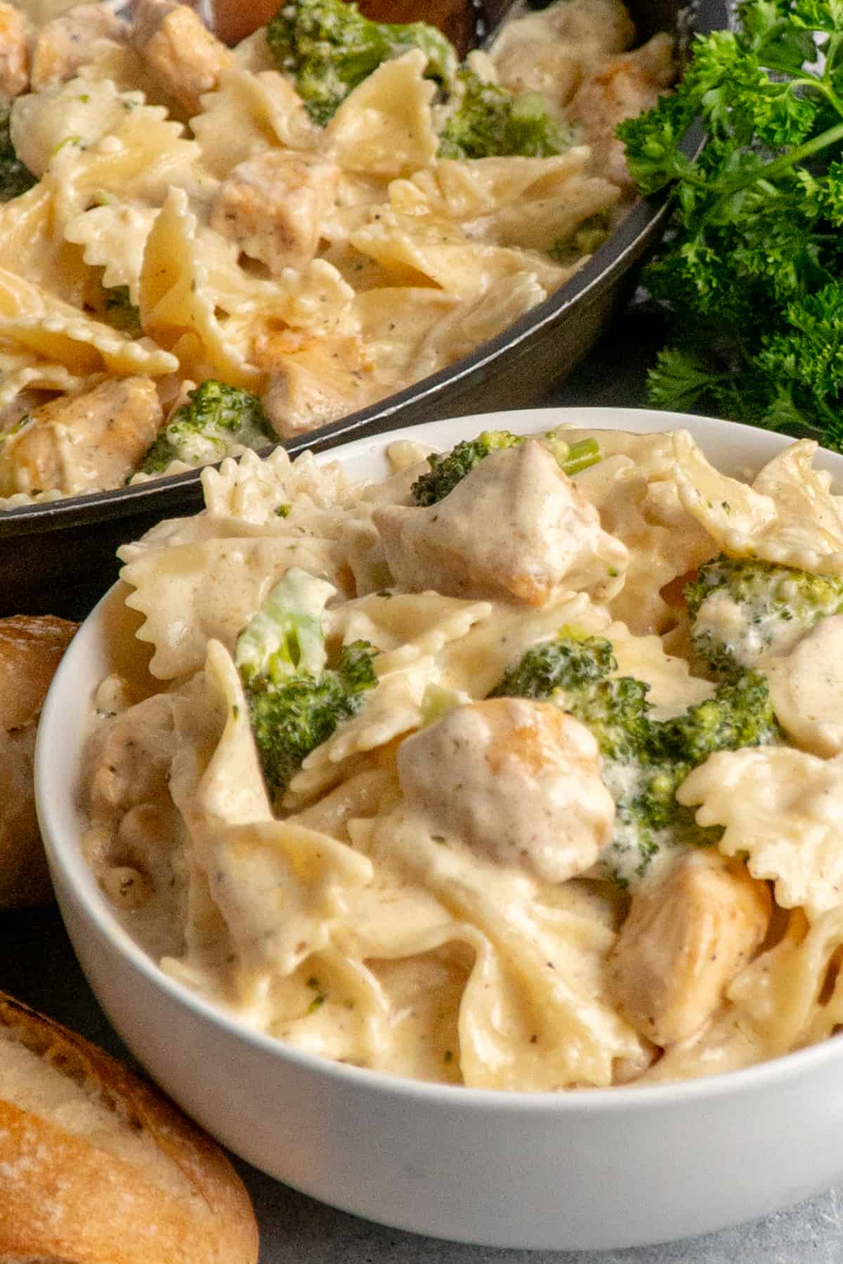 Close up of chicken Alfredo with broccoli in a white bowl.