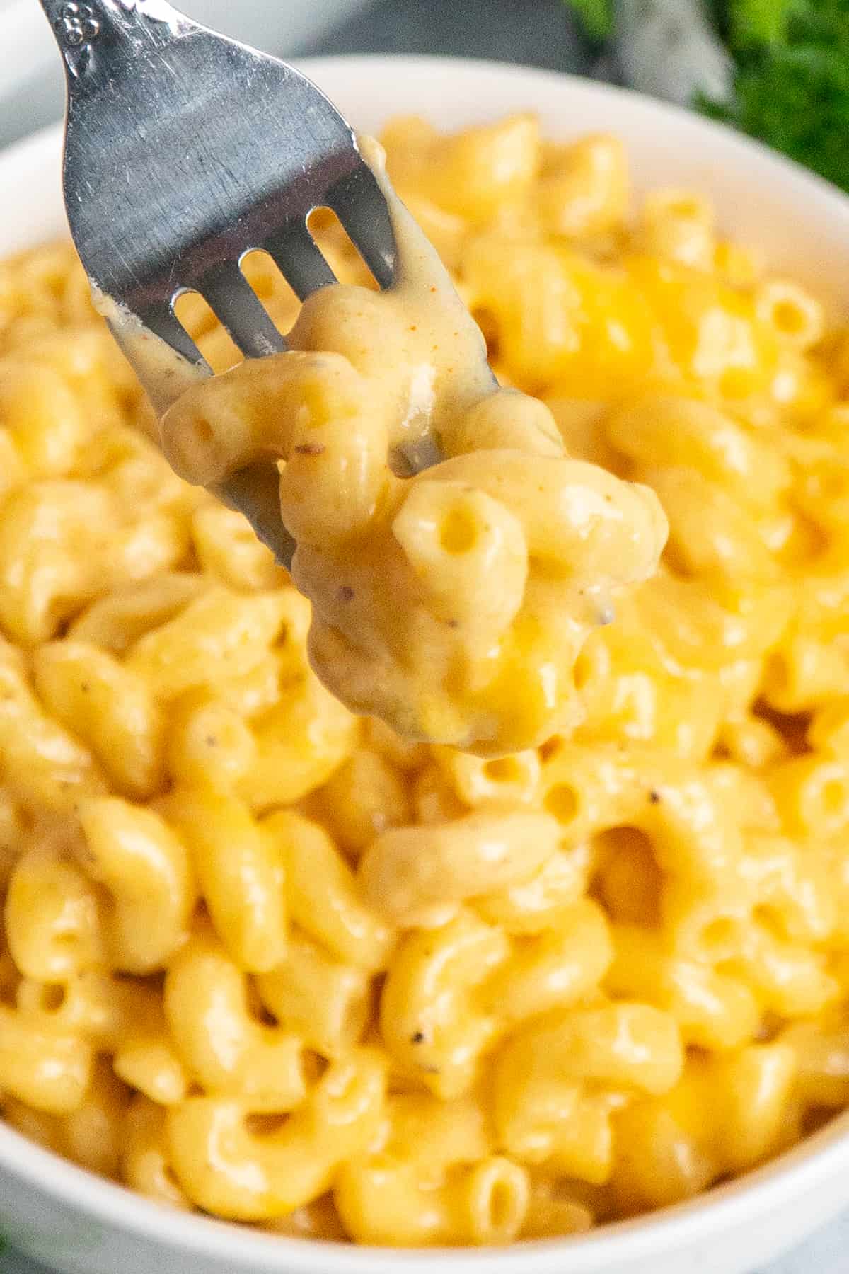 A fork holding a bit of mac and cheese over a bowl.