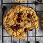 Chocolate chip cookies on a cooling rack with one in the center missing a bite.