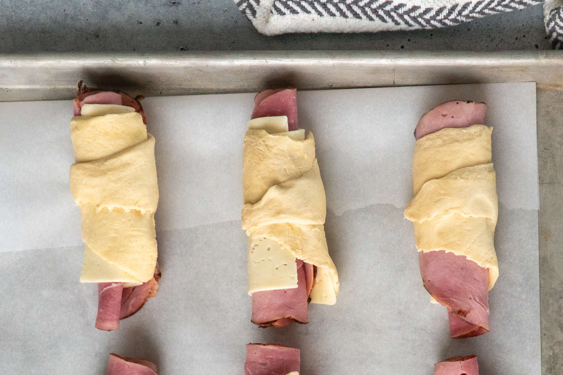Ham and cheese rolled up in crescent roll dough on a baking sheet.