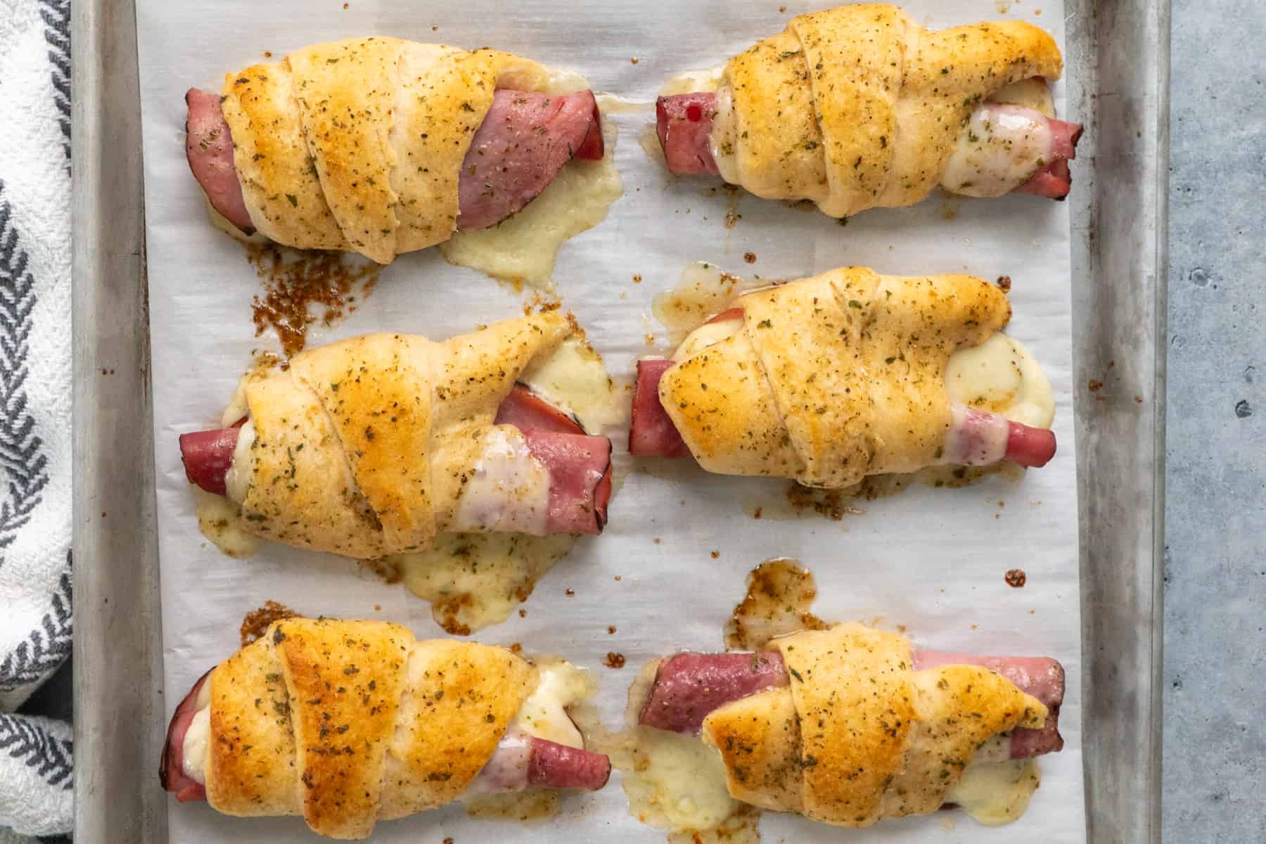 Baked ham and cheese crescent rolls on a baking sheet.