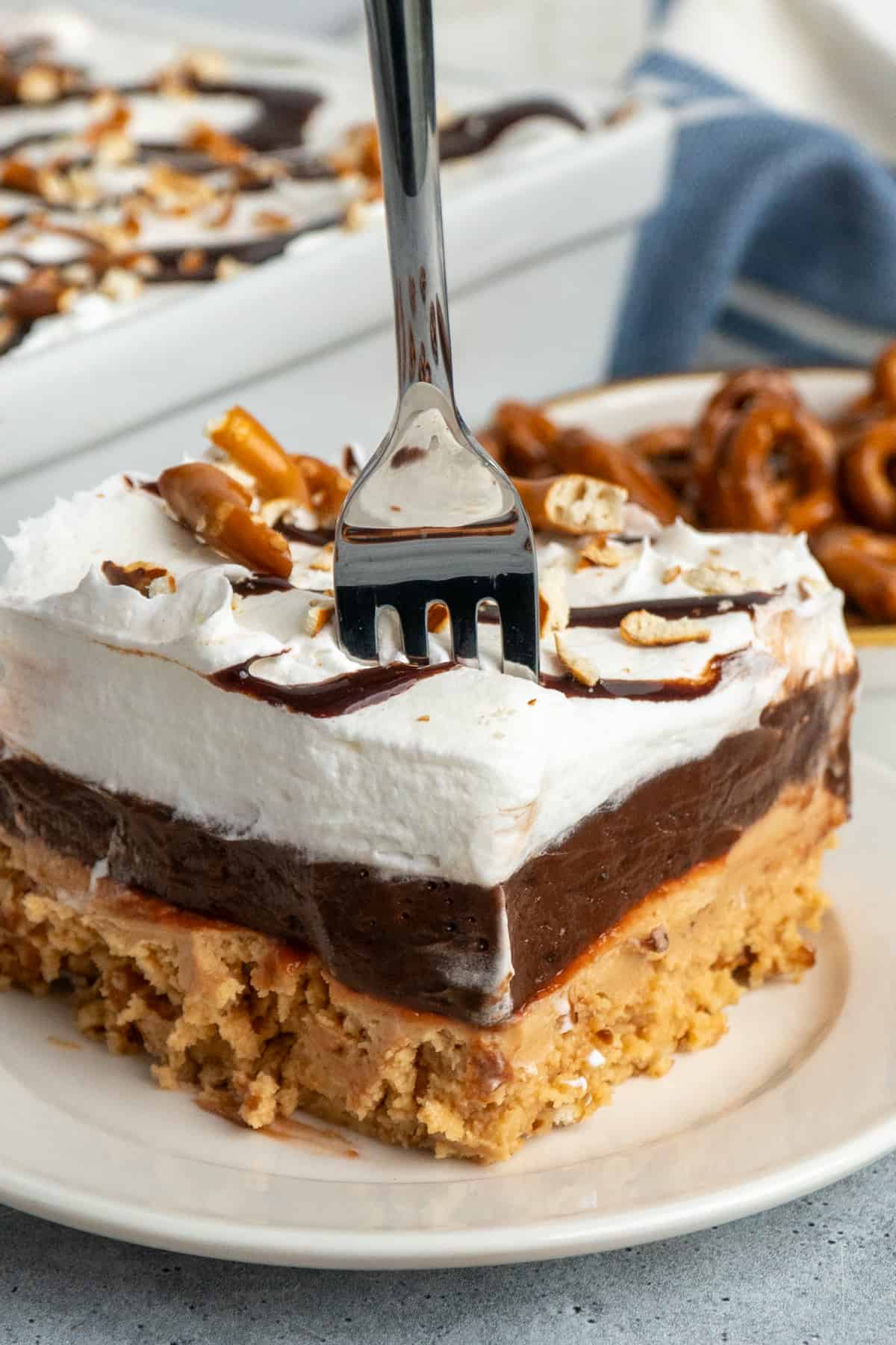 A fork in a slice of peanut butter pretzel pie on a white plate.