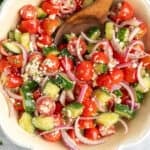Cucumber tomato salad in a bowl with a wooden spoon.