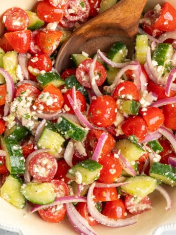 Cucumber tomato salad in a bowl with a wooden spoon.