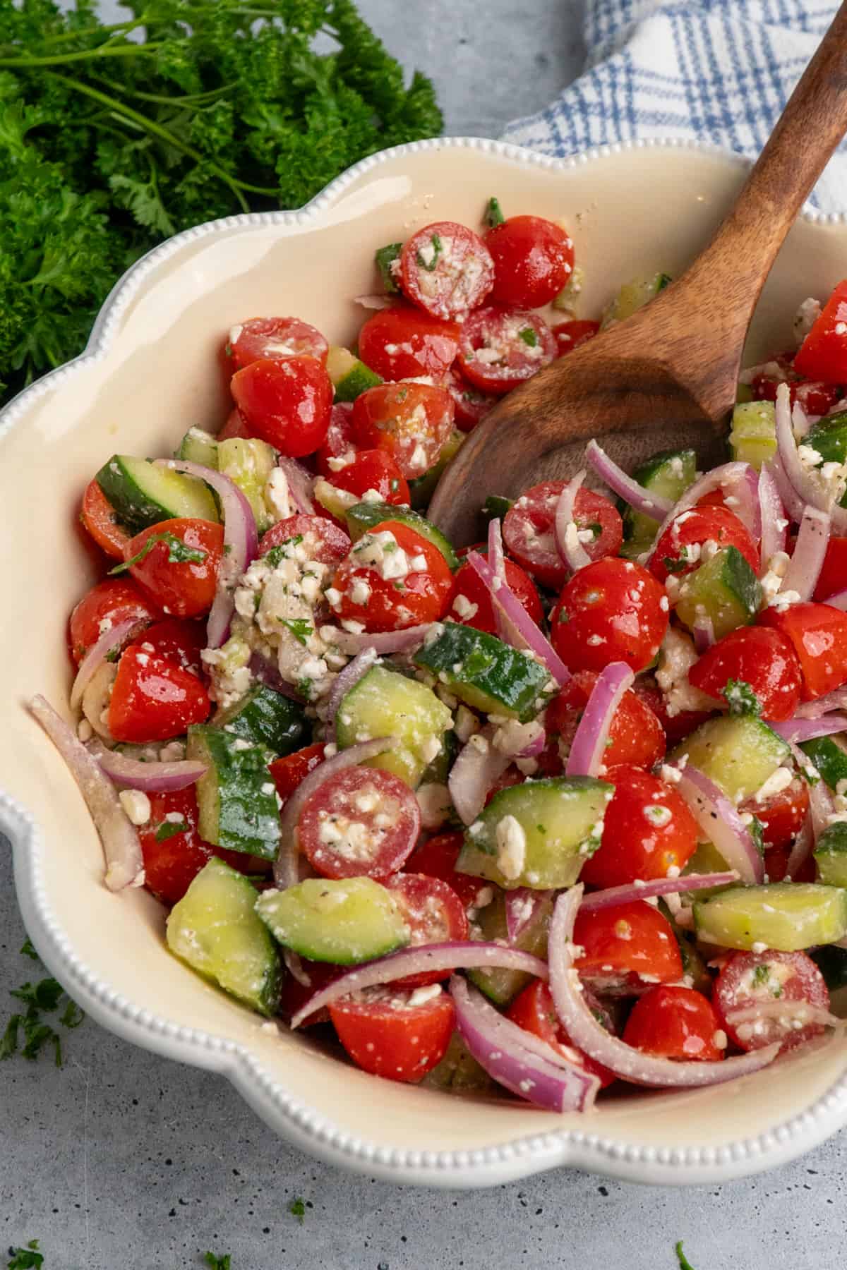 Cucumber tomato salad in a bowl with a wooden spoon in it.