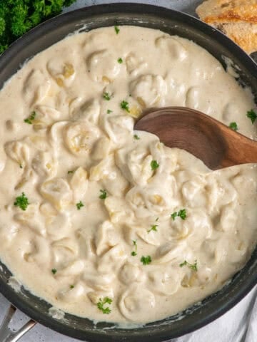 Tortellini Alfredo in a skillet with a wooden spoon resting in the dish.