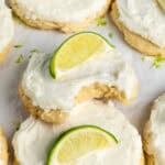 Coconut lime cookies on parchment paper with one that has a bite take out of it.