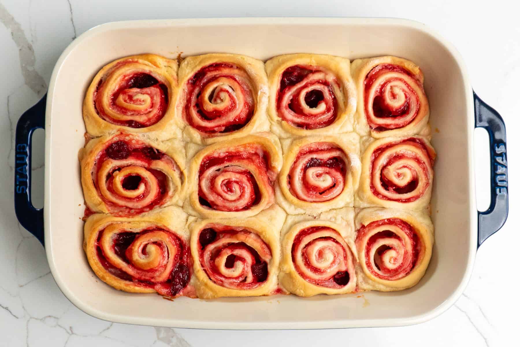 Overhead look at baked strawberry cheesecake cinnamon rolls in a baking dish.