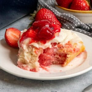 Close up of a strawberry cheesecake cinnamon roll with a bite taken out of it.