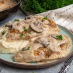 Close up of chicken and mushroom over mashed potatoes on a plate.
