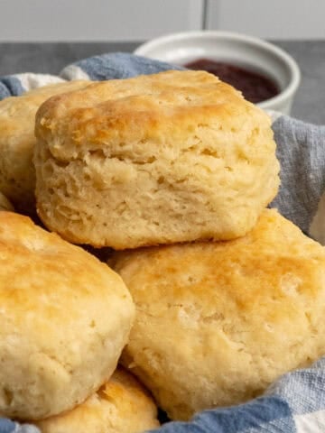 Homemade biscuits stacked up in a bread basket.