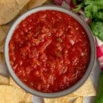 Restaurant style salsa in a bowl with tortilla chips around it.