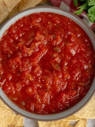 Restaurant style salsa in a bowl with tortilla chips around it.