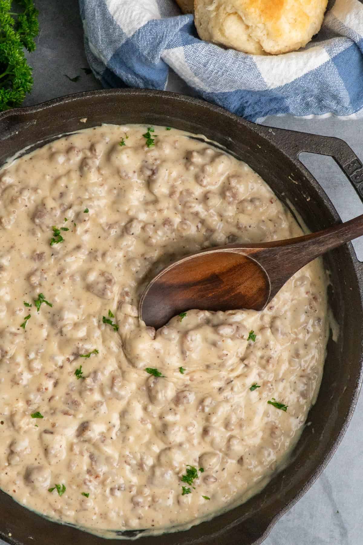 Sausage gravy in a cast iron skillet with a wooden spoon in it.