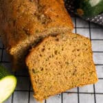 Zucchini bread on a cooling rack with a slice cut off.