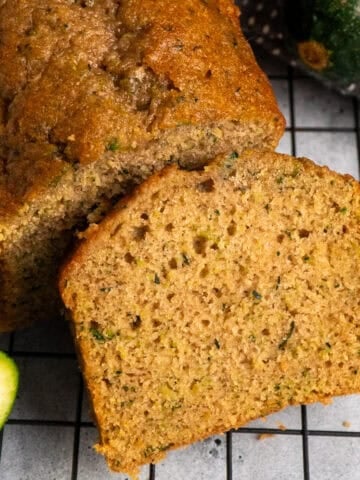Zucchini bread on a cooling rack with a slice cut off.