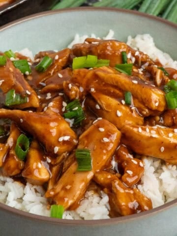 Bourbon chicken over a bowl of rice and garish with green onions.