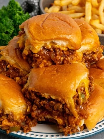 Sloppy Joe slides stacked up on a plate with fries in the background.