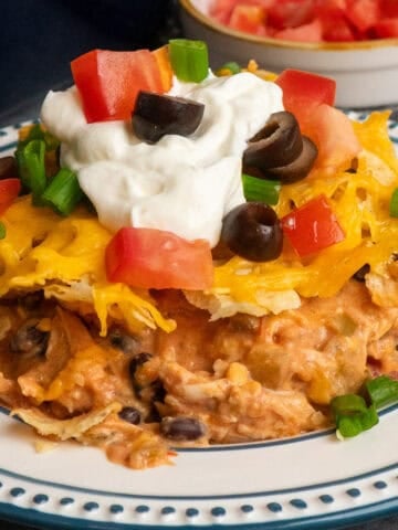 Chicken taco casserole on a plate topped with sour cream and toppings.
