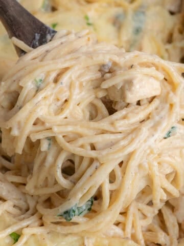 A wooden spoon lifting up a serving of chicken tetrazzini from the casserole dish.