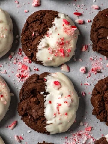 Chocolate peppermint cookies on parchment paper surrounded by crushed candy canes.