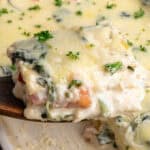 A wooden spatula holding a piece of chicken alfredo lasagna.
