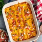 Ground beef enchiladas in a baking dish and topped with Pico de Gallo.