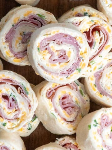 Ham and cheese roll ups stacked on a plate.