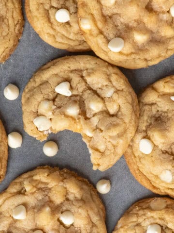 White chocolate & macadamia nut cookies on a counter top with that has a bite taken out of it.
