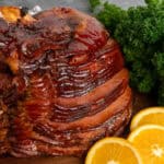 Baked ham covered in a brown sugar glaze on a wood cutting board.