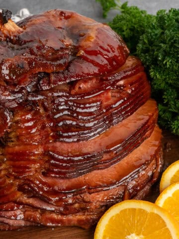 Baked ham covered in a brown sugar glaze on a wood cutting board.