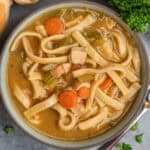 A bowl of chicken noodle soup with egg noodles on the table.