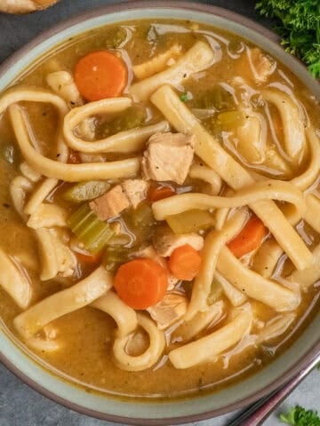 A bowl of chicken noodle soup with egg noodles on the table.