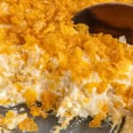 Funeral potatoes in a casserole dish with a wooden spoon starting to scoop some up.