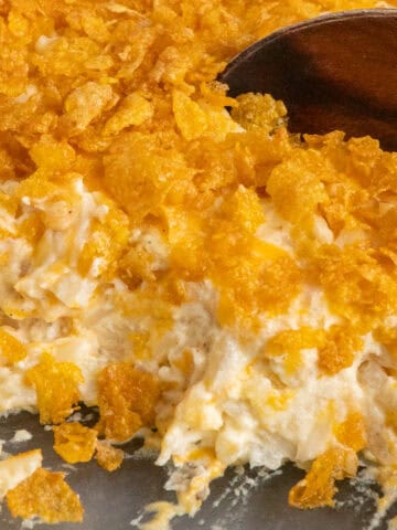 Funeral potatoes in a casserole dish with a wooden spoon starting to scoop some up.