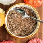 A bowl of hamburger seasoning on the table with a spoon on the dish.