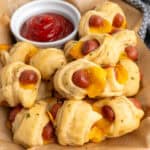 Crescent roll pigs in a blanket on a basket with a bowl of ketchup.