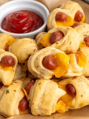 Crescent roll pigs in a blanket on a basket with a bowl of ketchup.